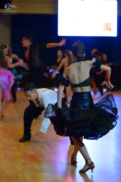 Dancesport competitor: Female dancer (foreground): black sequined crop top and a voluminous, tiered bla