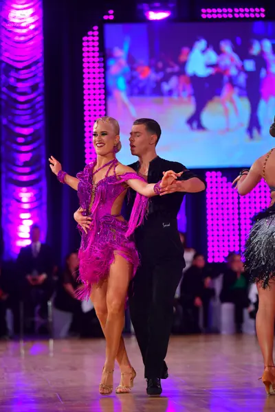Dancesport competitor: Female dancer: magenta Latin dance dress with sequins and long fringe, and a mat