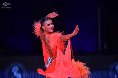 Dancesport competitor: Female dancer: bright orange latin dress with feather accents on the sleeves and