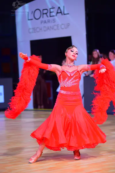 Dancesport competitor: Female dancer: red Latin dress with a sequined bodice, long sleeves, and volumin