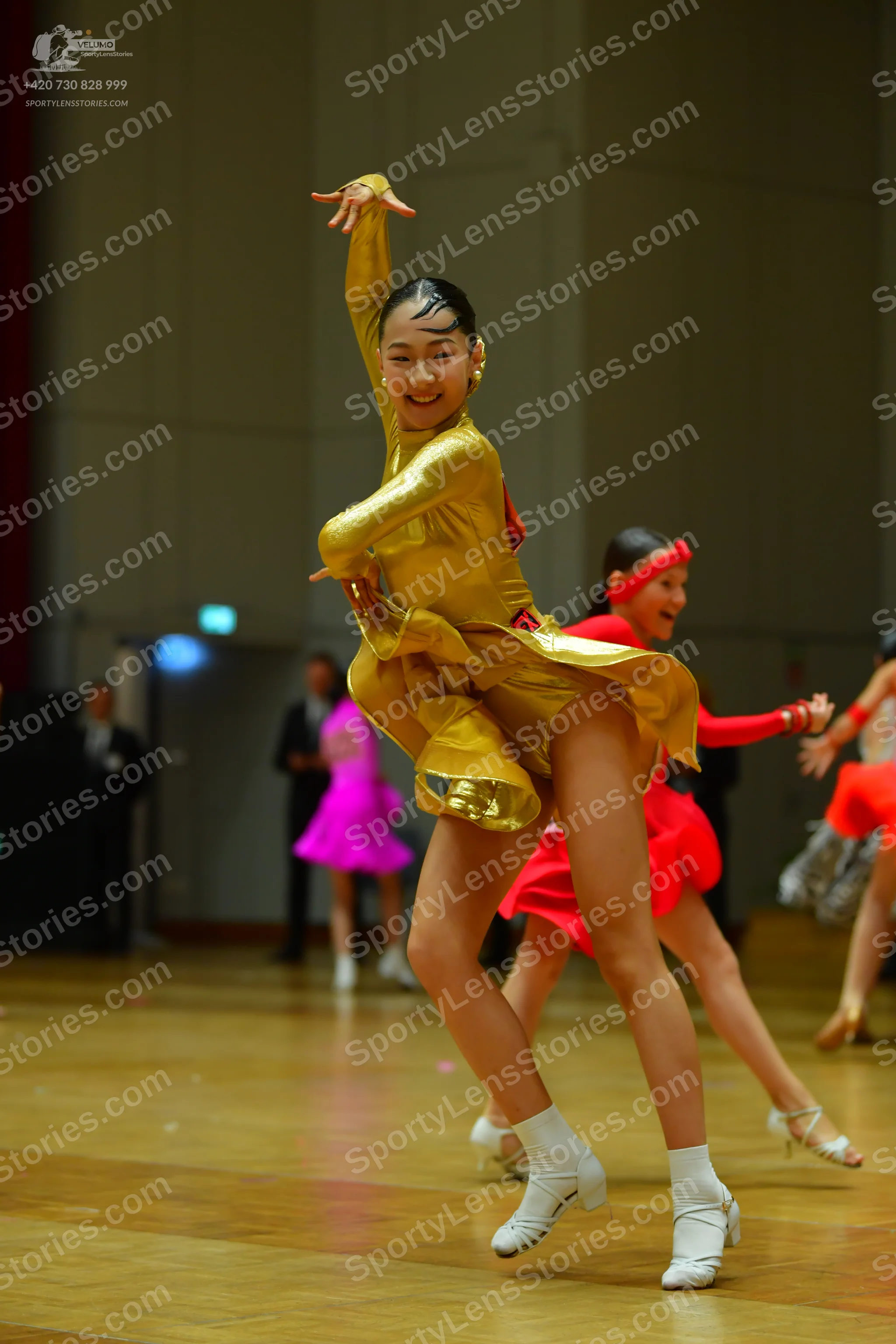 Dancesport competitor: Female dancer in foreground: gold metallic latin dress with long sleeves and a s