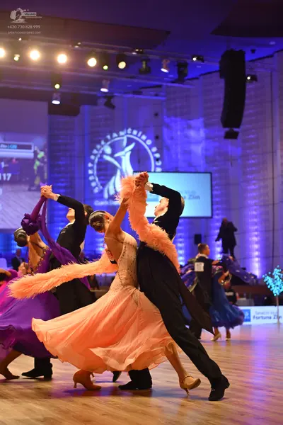 Dancesport competitor: Foreground female dancer: peach-colored ballgown with a lace or sequined bodice 