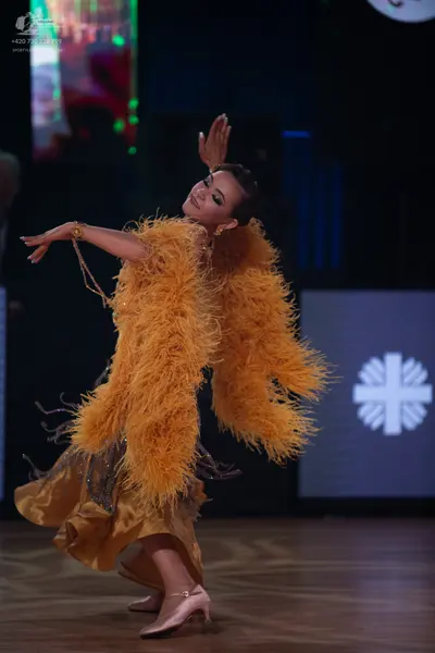 Dancesport competitor: Female dancer: mustard yellow Latin dance dress with voluminous feather embellis
