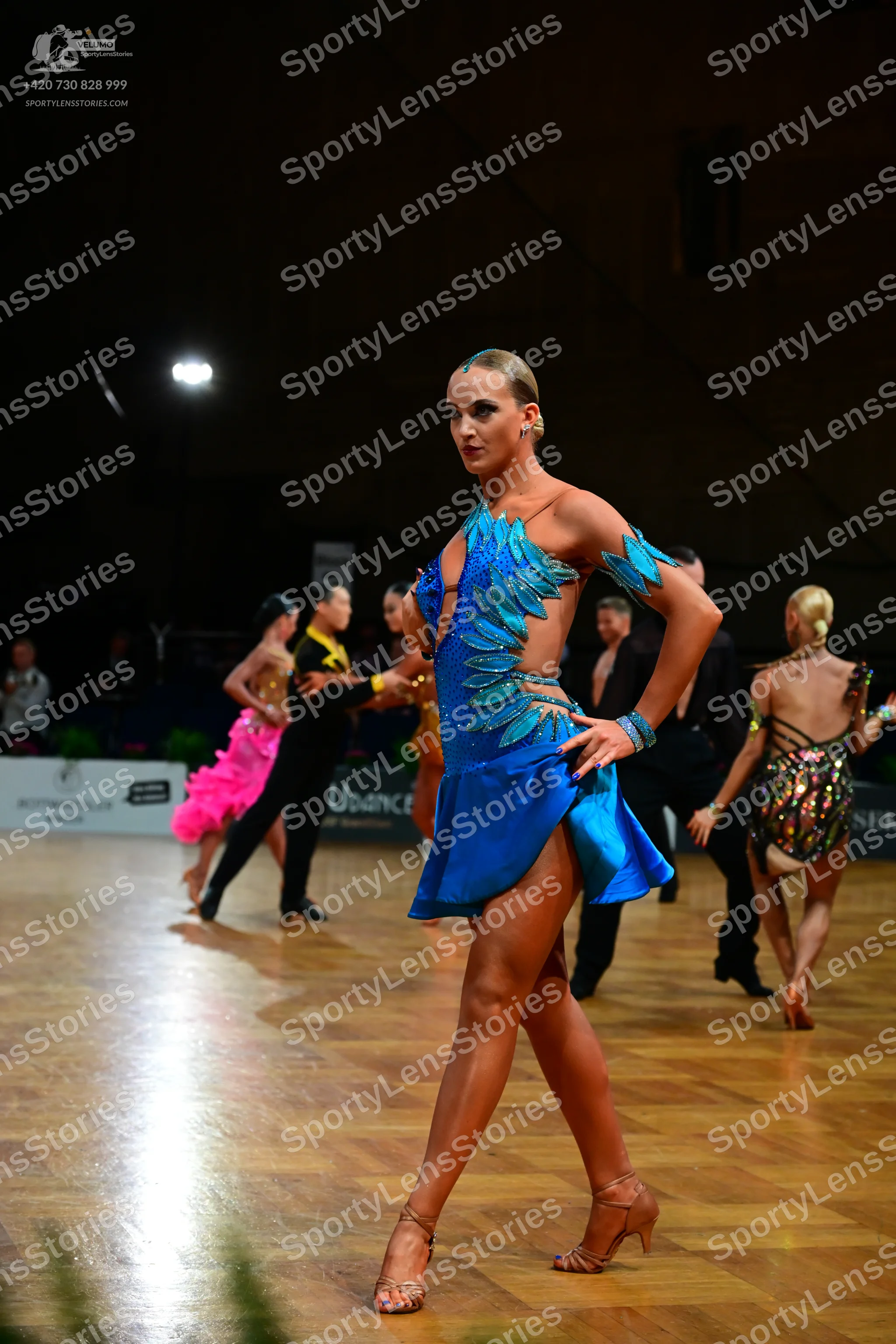 Dancesport competitor: Foreground female dancer: blue Latin dance dress with teal/light blue sequined o
