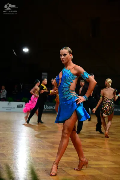 Dancesport competitor: Foreground female dancer: blue Latin dance dress with teal/light blue sequined o