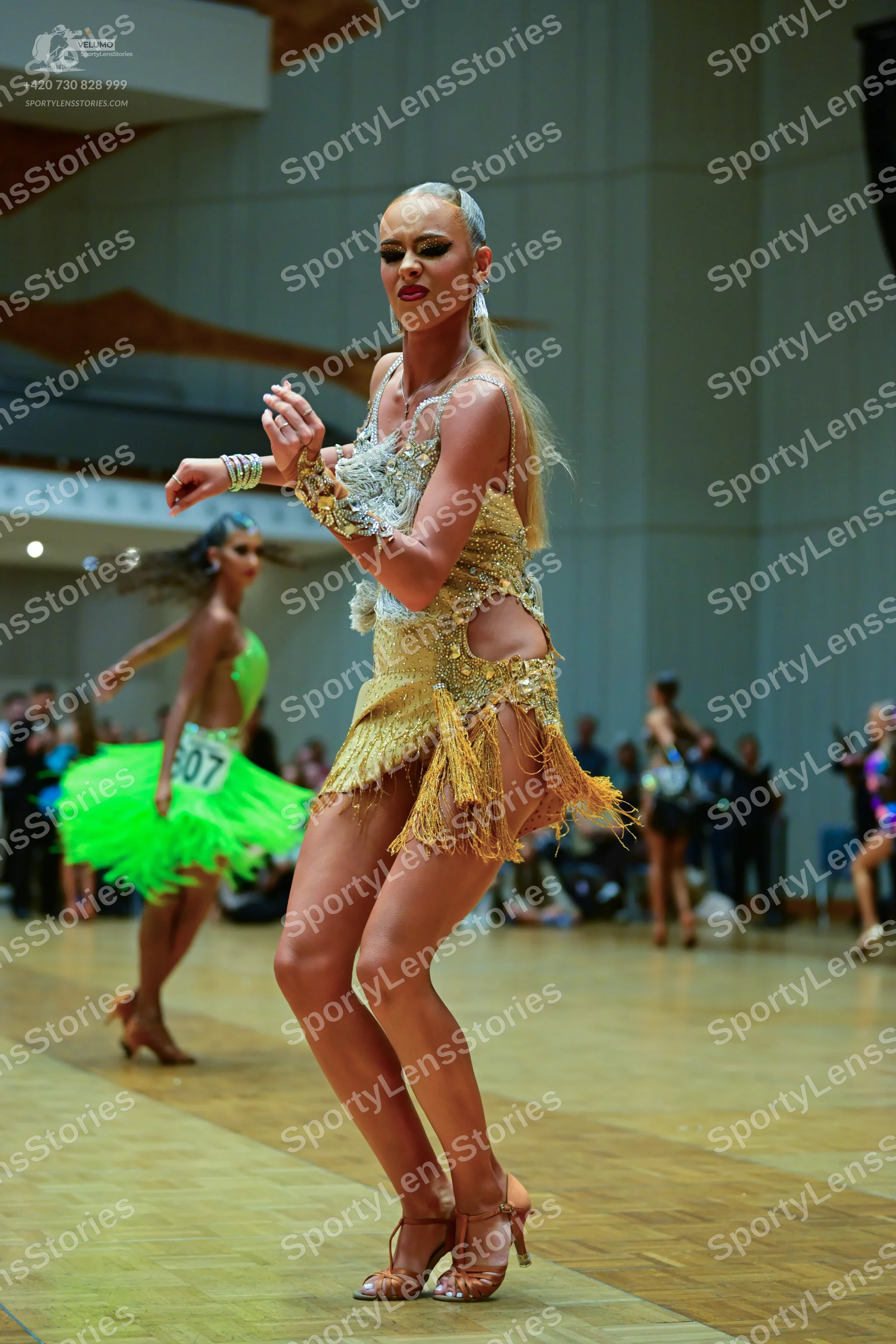 Dancesport competitor #607: Female dancer (foreground): gold latin dress with sequins, lace, and fringe, pai