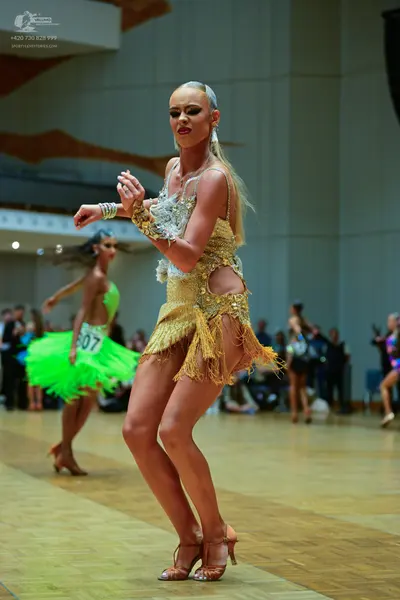 Dancesport competitor #607: Female dancer (foreground): gold latin dress with sequins, lace, and fringe, pai