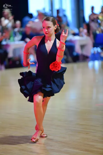 Dancesport competitor: Female dancer: dark navy Latin dance dress with a ruffled skirt, a red fabric fl