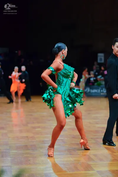 Dancesport competitor: Main female dancer: green sequined Latin dress with a ruffled skirt and large gr