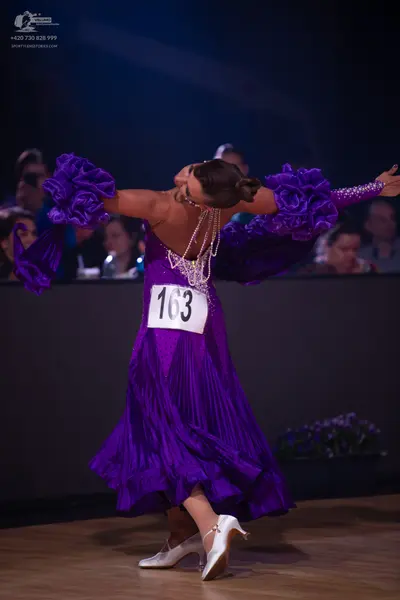 Dancesport competitor: Female dancer: purple ballroom dress with large ruffled sleeves and sparkly trim