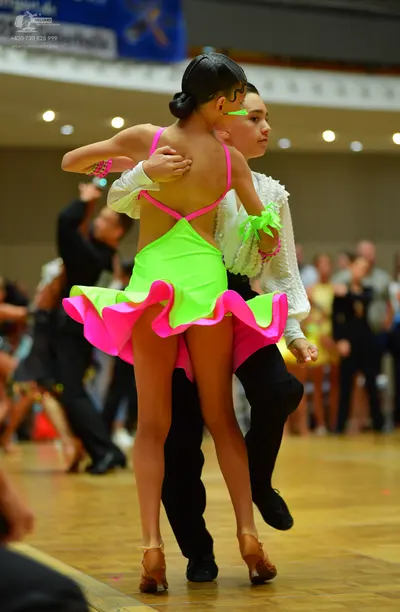 Dancesport competitor: Female dancer: neon green latin dress with bright pink ruffled skirt edge and pi