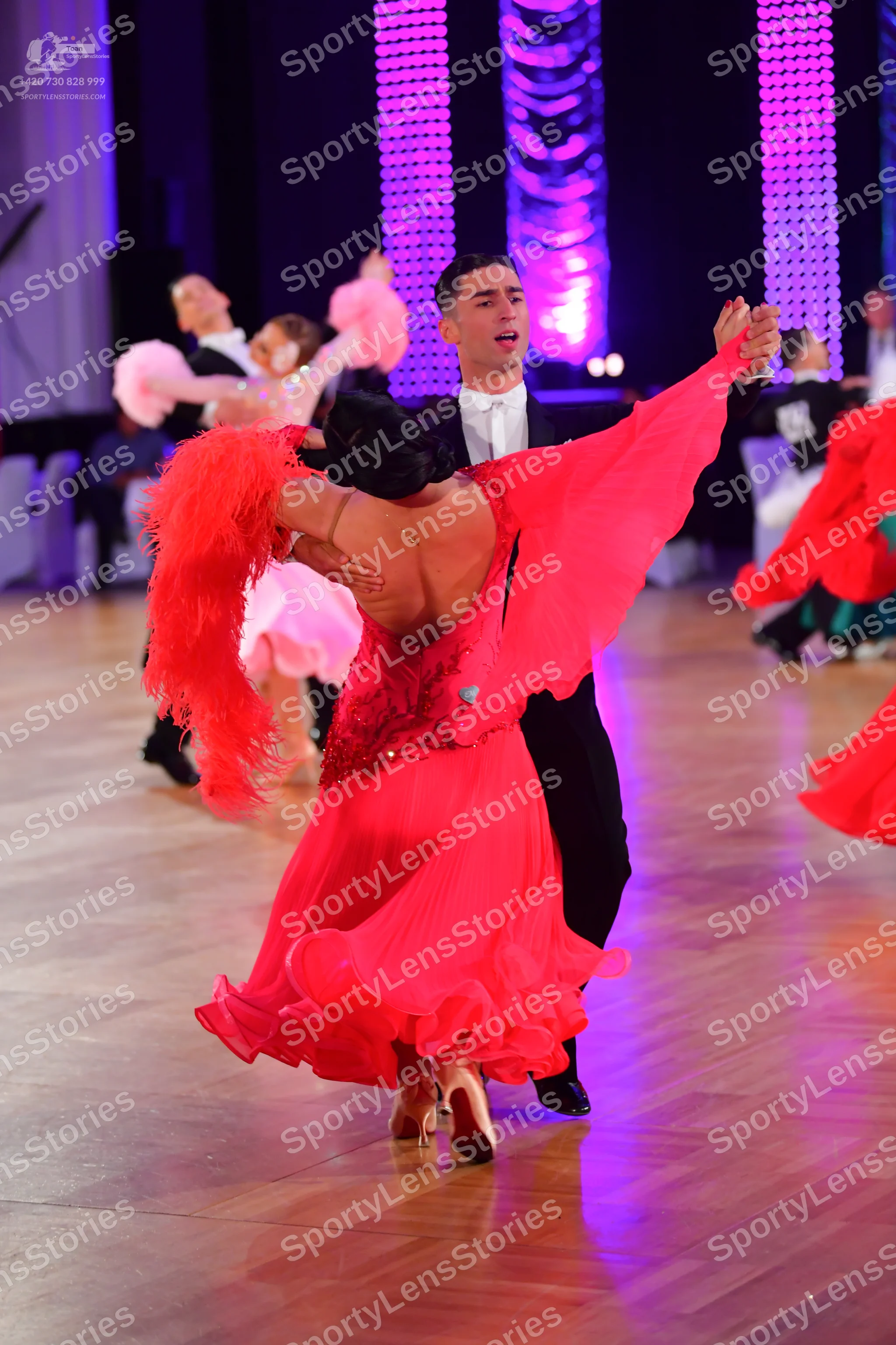 Dancesport competitor: Foreground female dancer: red Latin dress with long red fringe