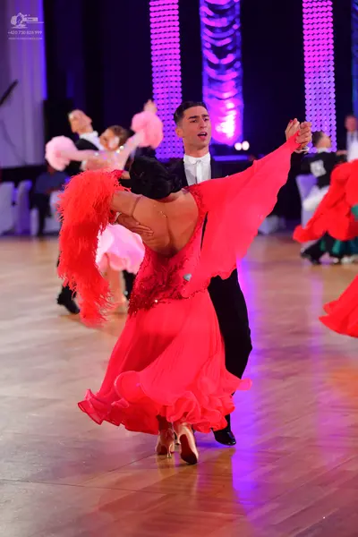 Dancesport competitor: Foreground female dancer: red Latin dress with long red fringe