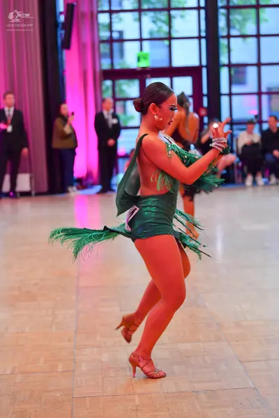 Dancesport competitor: Female dancer in foreground: emerald green latin dress with fringe and shiny fab