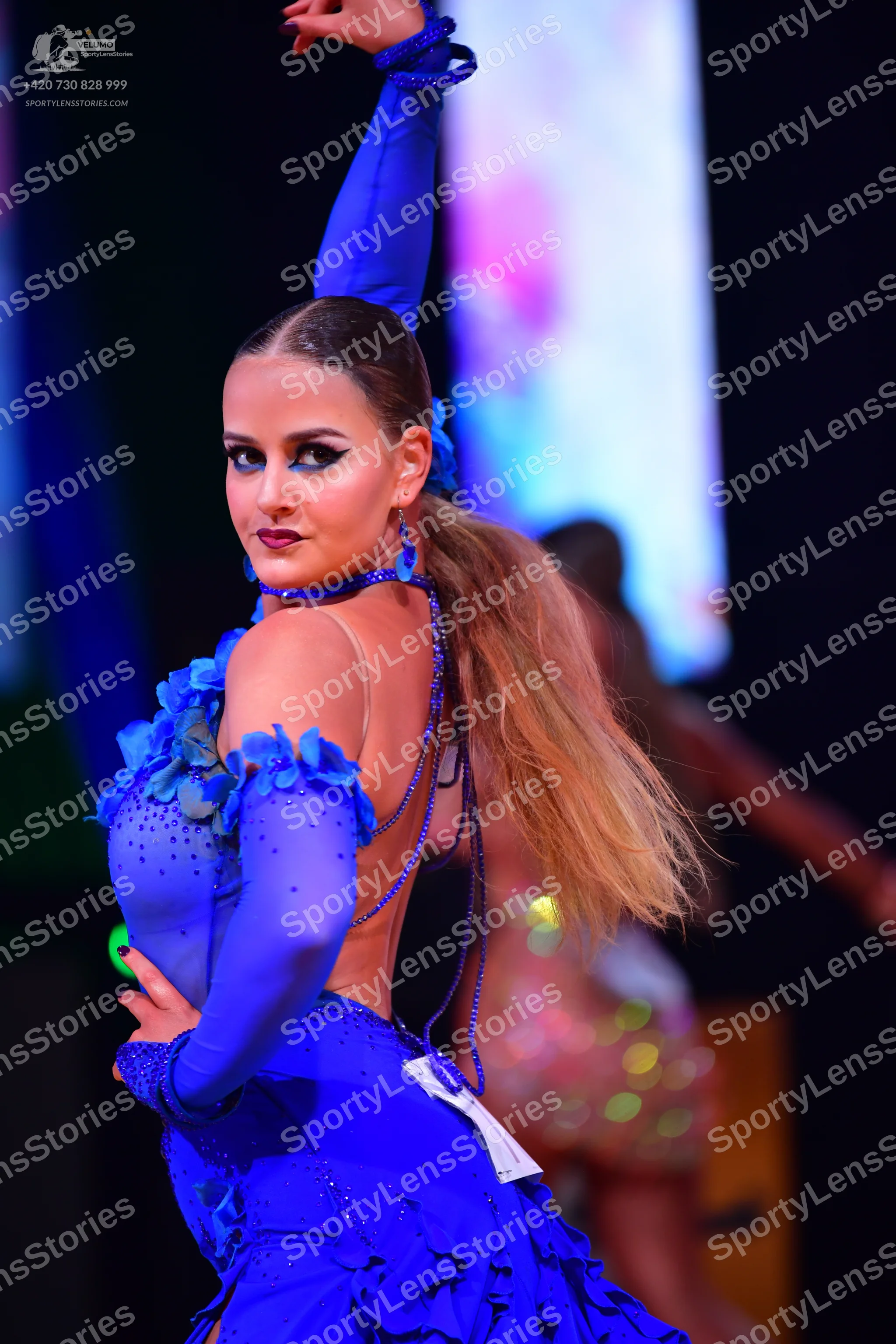 Dancesport competitor: Female dancer (foreground): bright blue, long-sleeved Latin dance dress with ruf