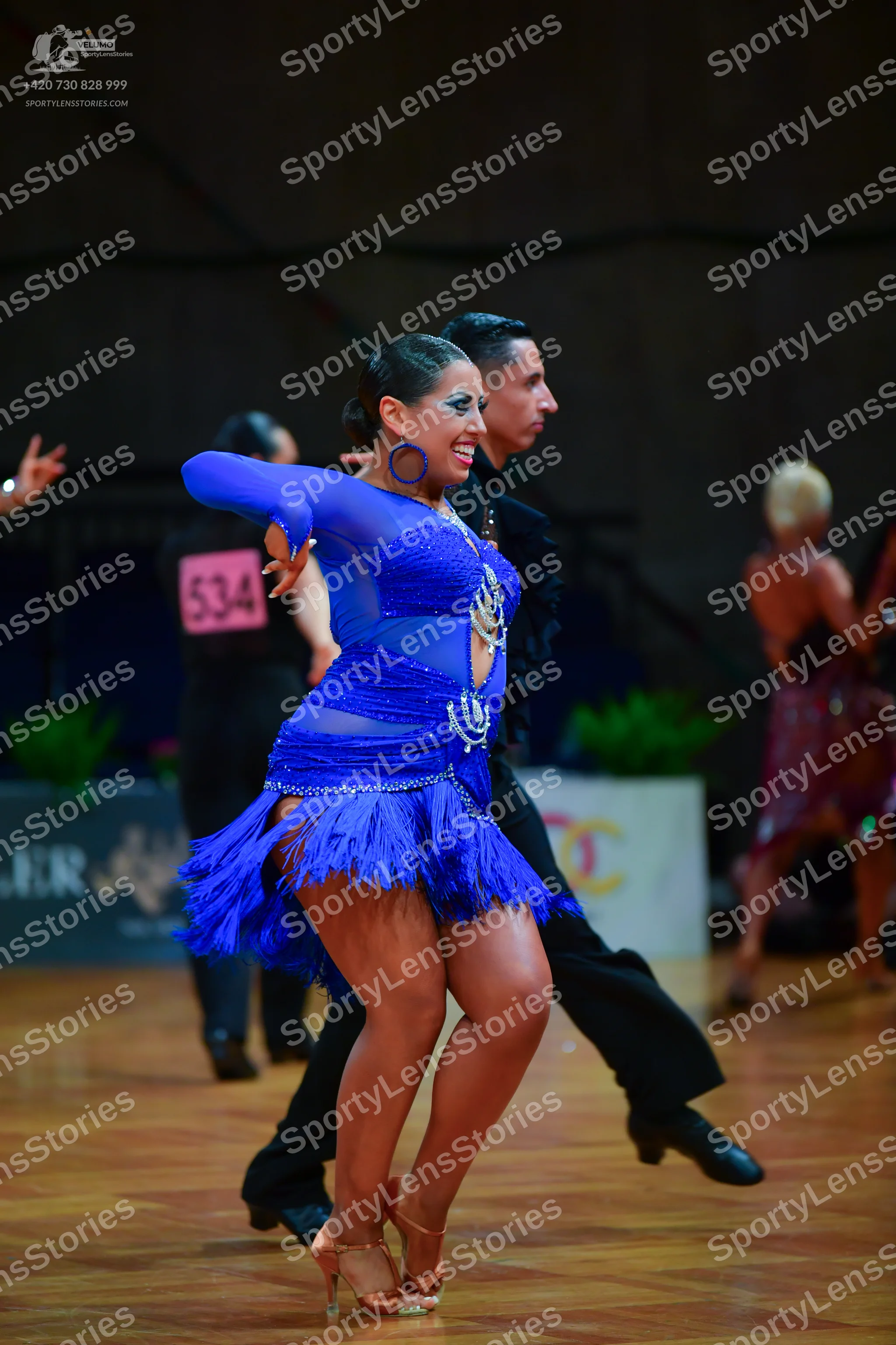Dancesport competitor: Female dancer: blue latin dress with sequins, mesh panels, and fringe; blue hoop