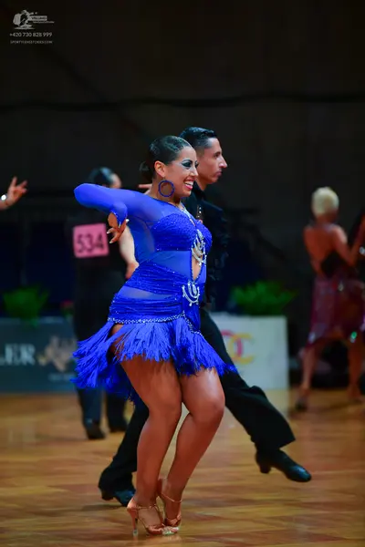 Dancesport competitor: Female dancer: blue latin dress with sequins, mesh panels, and fringe; blue hoop