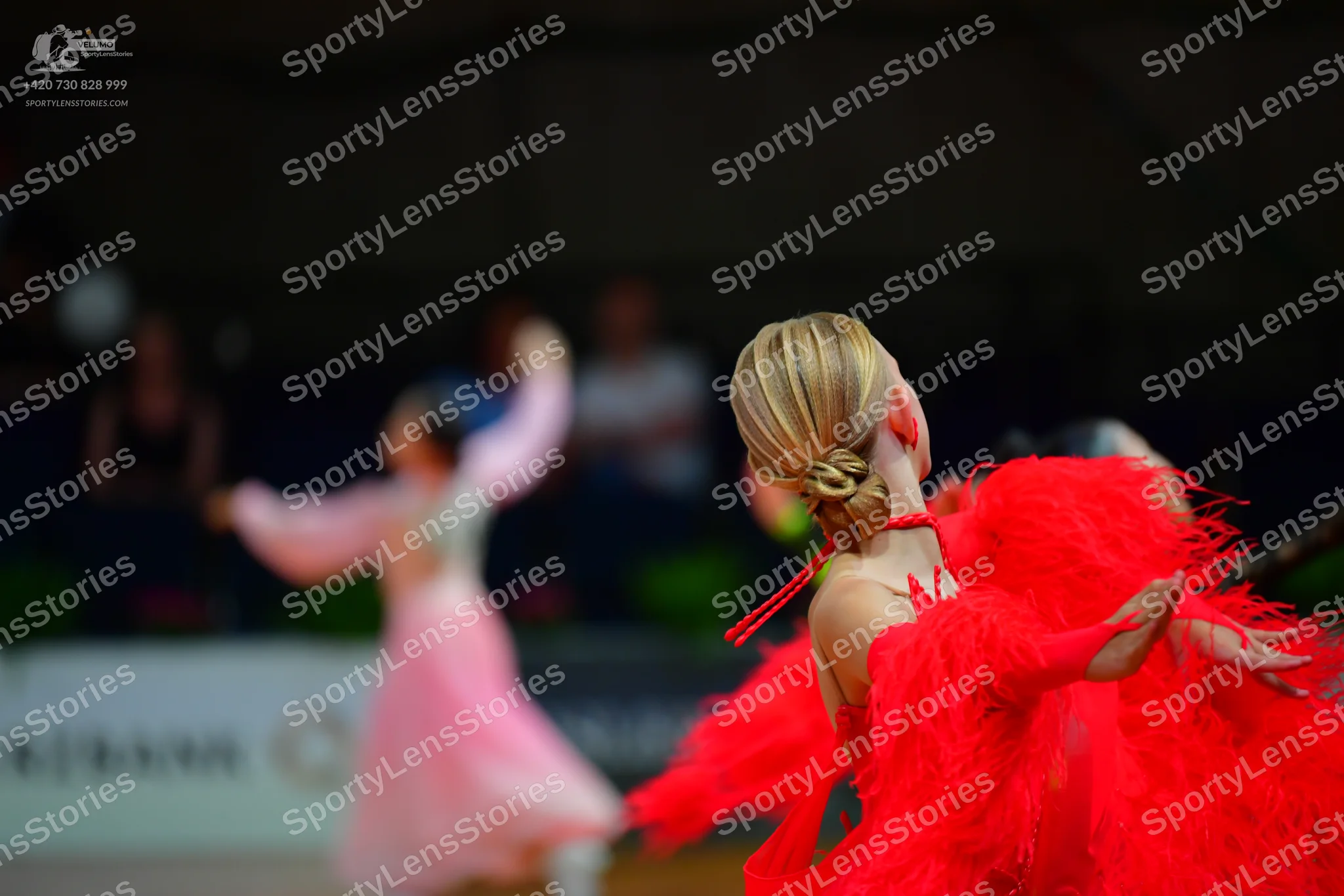 Dancesport competitor: Female dancer in foreground: bright red latin dress with voluminous fringe or ru