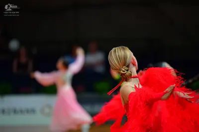 Dancesport competitor: Female dancer in foreground: bright red latin dress with voluminous fringe or ru