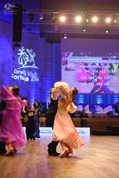 Dancesport competitor: Female dancer (left): purple, flowing, multi-layered chiffon ballgown