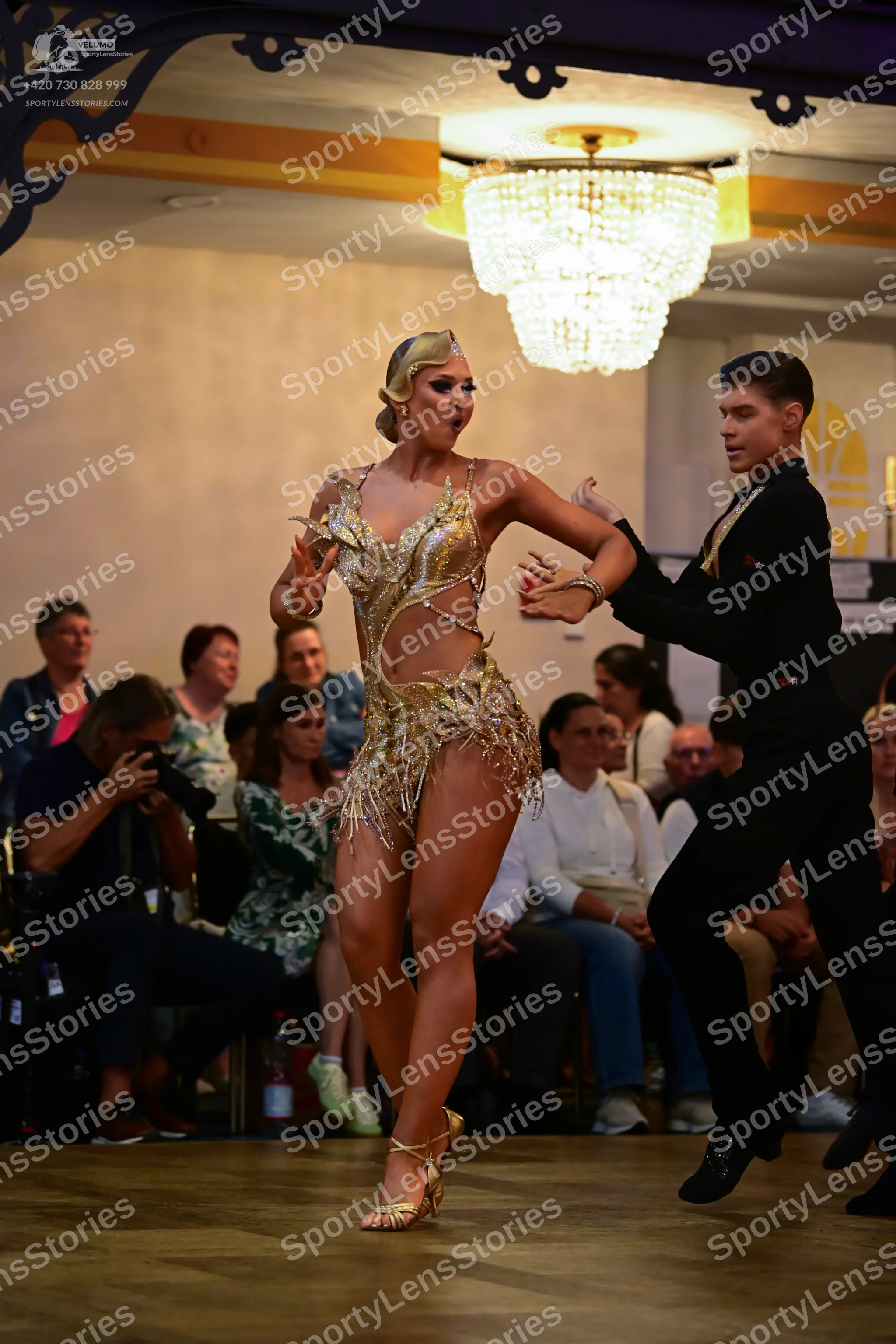 Dancesport competitor: Female dancer: gold Latin dance dress with cut-outs and metallic/sequin texture,