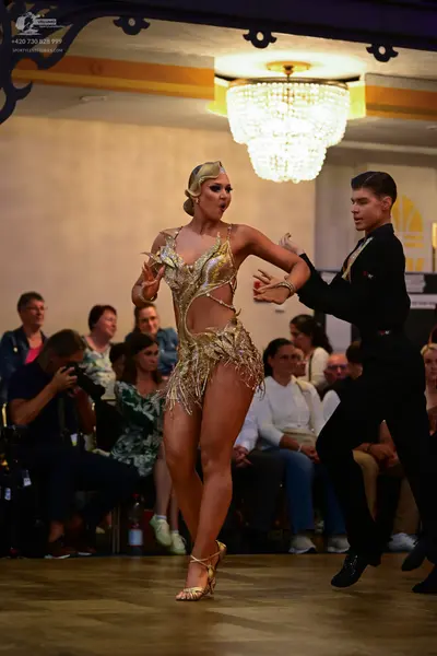 Dancesport competitor: Female dancer: gold Latin dance dress with cut-outs and metallic/sequin texture,