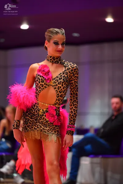 Dancesport competitor: Female dancer: leopard print latin dress with long sleeves, cutouts, pink feathe