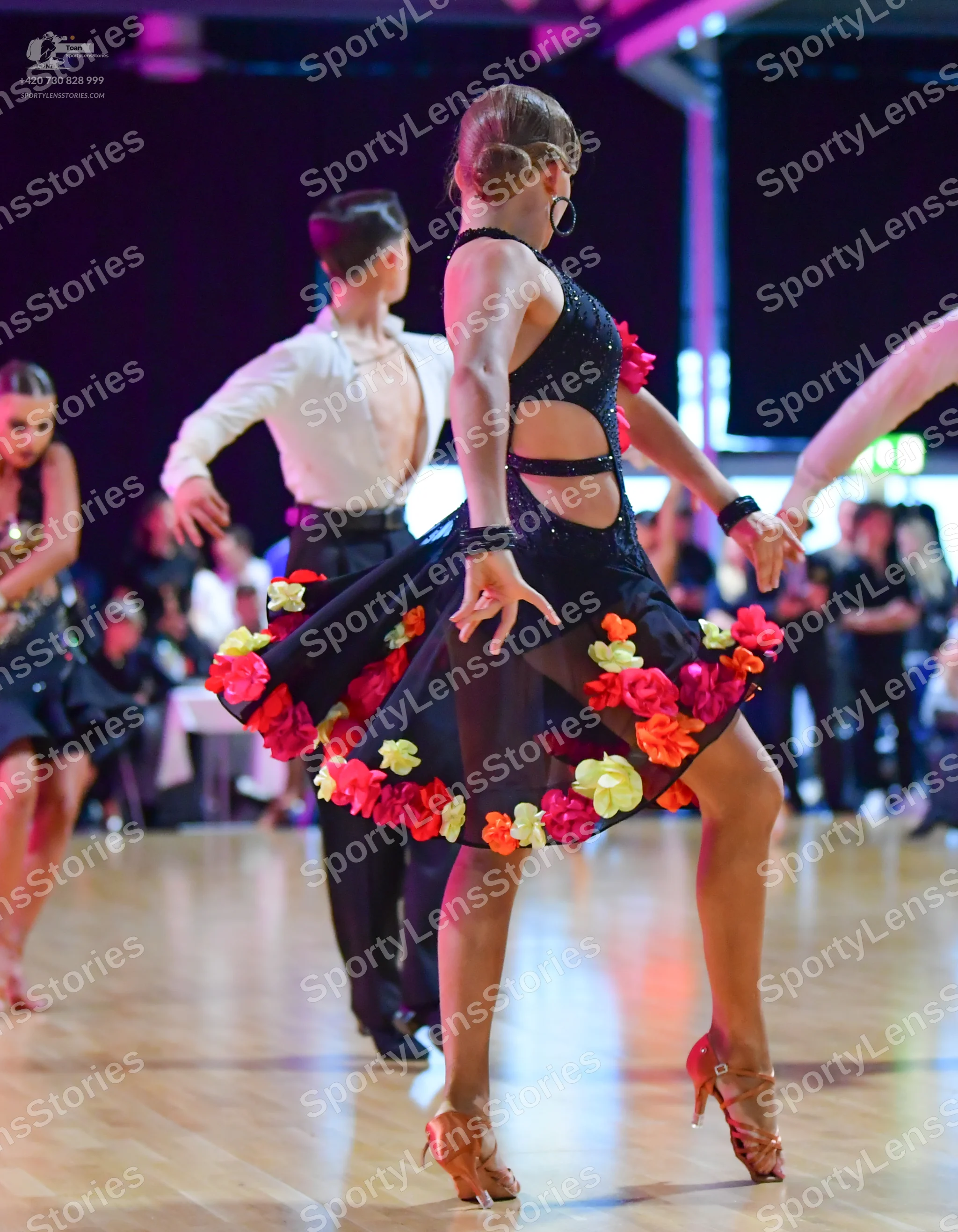 Dancesport competitor: Female dancer in foreground: black latin dress with side cut-outs and colorful f