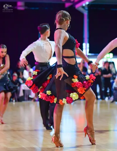 Dancesport competitor: Female dancer in foreground: black latin dress with side cut-outs and colorful f
