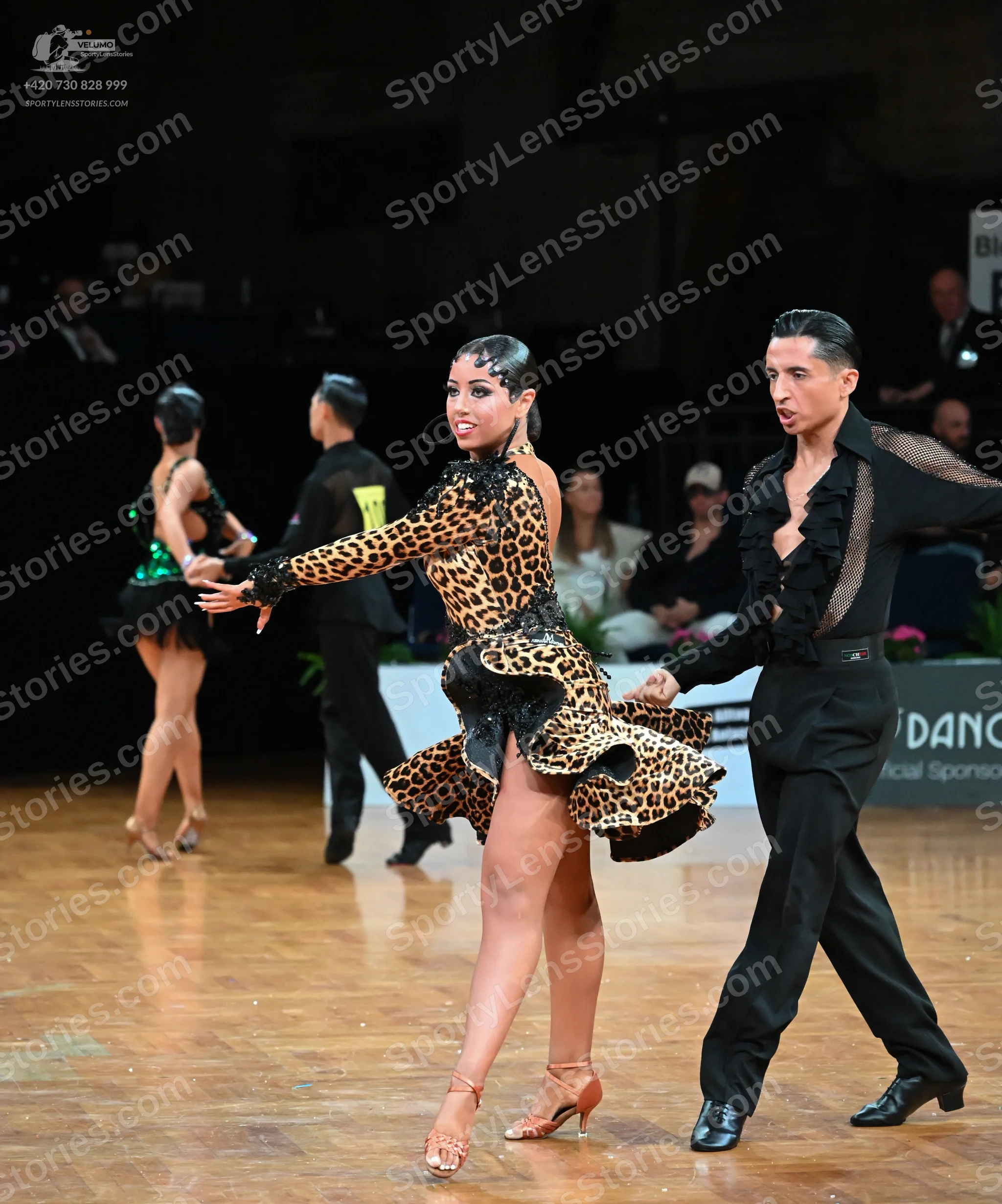 Dancesport competitor: Female dancer (foreground): leopard print Latin dress with long sleeves and a ru