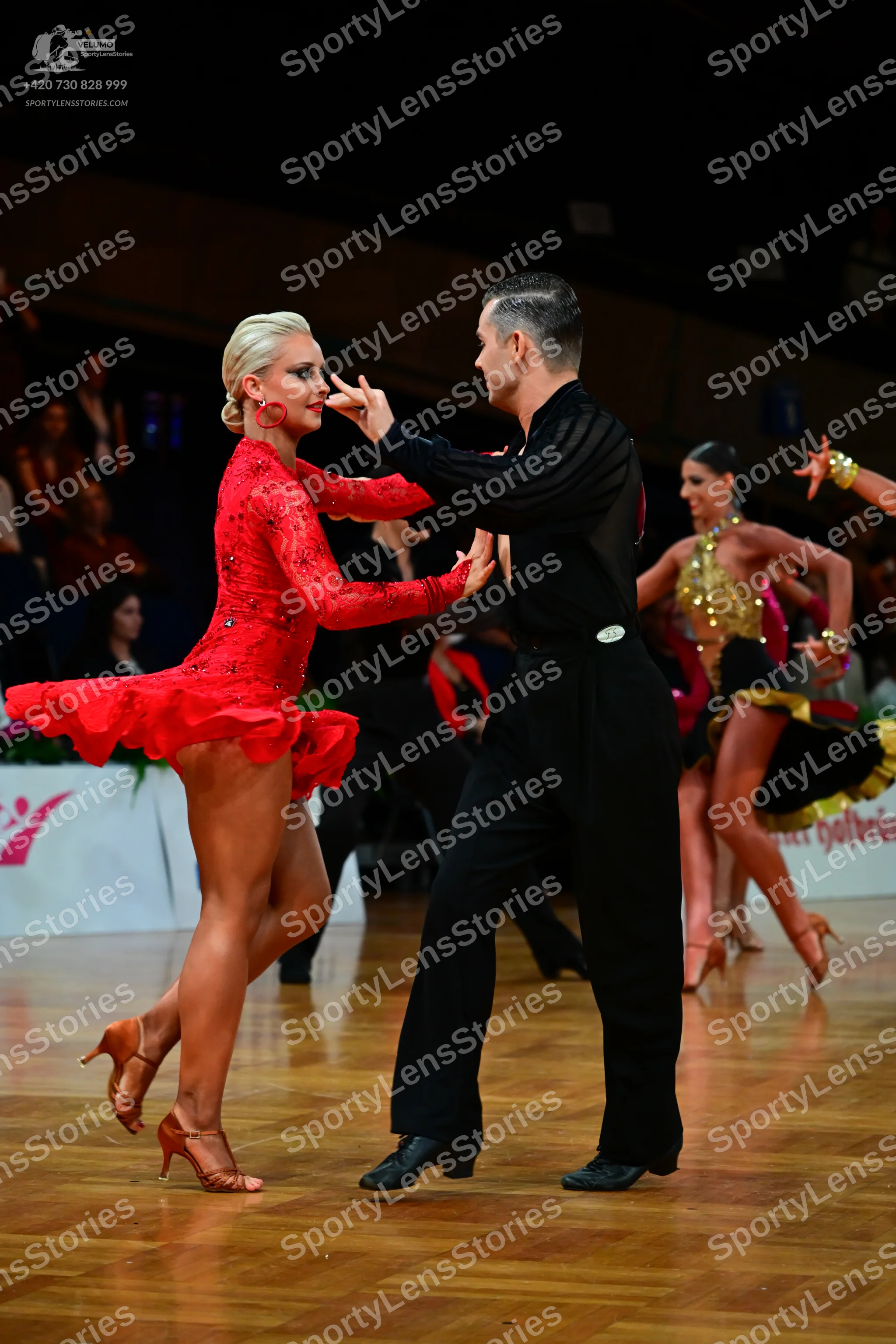 Dancesport competitor: Female dancer in foreground: red long-sleeved lace Latin dress with a ruffled sk