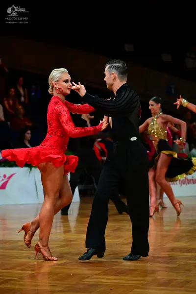 Dancesport competitor: Female dancer in foreground: red long-sleeved lace Latin dress with a ruffled sk