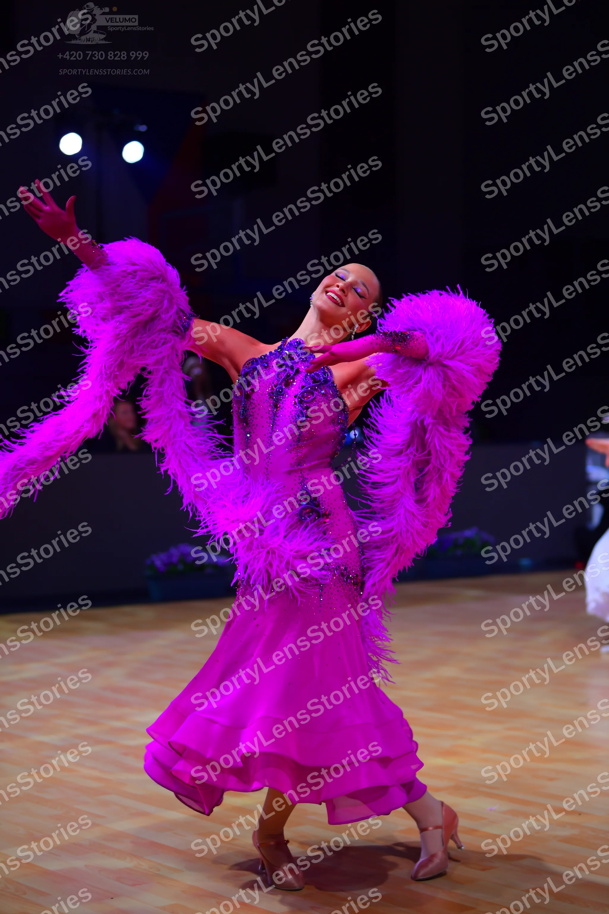 Dancesport competitor: Female dancer: bright pink latin dress with large feather attachments on the arm