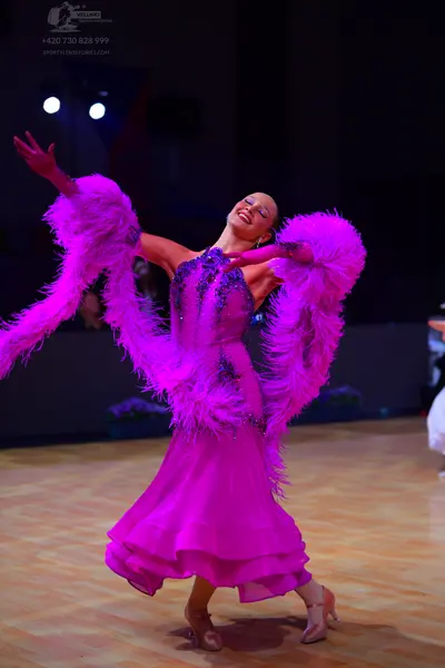 Dancesport competitor: Female dancer: bright pink latin dress with large feather attachments on the arm