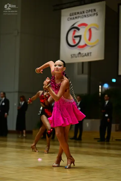 Dancesport competitor: Female dancer in foreground: bright pink sequined Latin dress with cut-outs and 