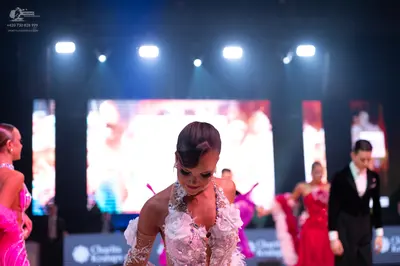 Dancesport competitor: Female dancer in foreground: white/cream dress with intricate floral lace appliq