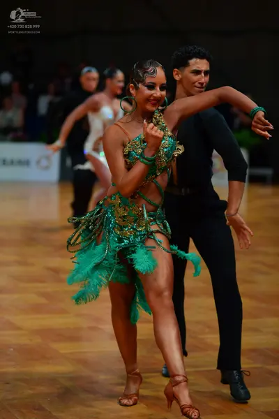 Dancesport competitor: Lead female dancer: emerald green Latin dance dress with gold sequin embellishme