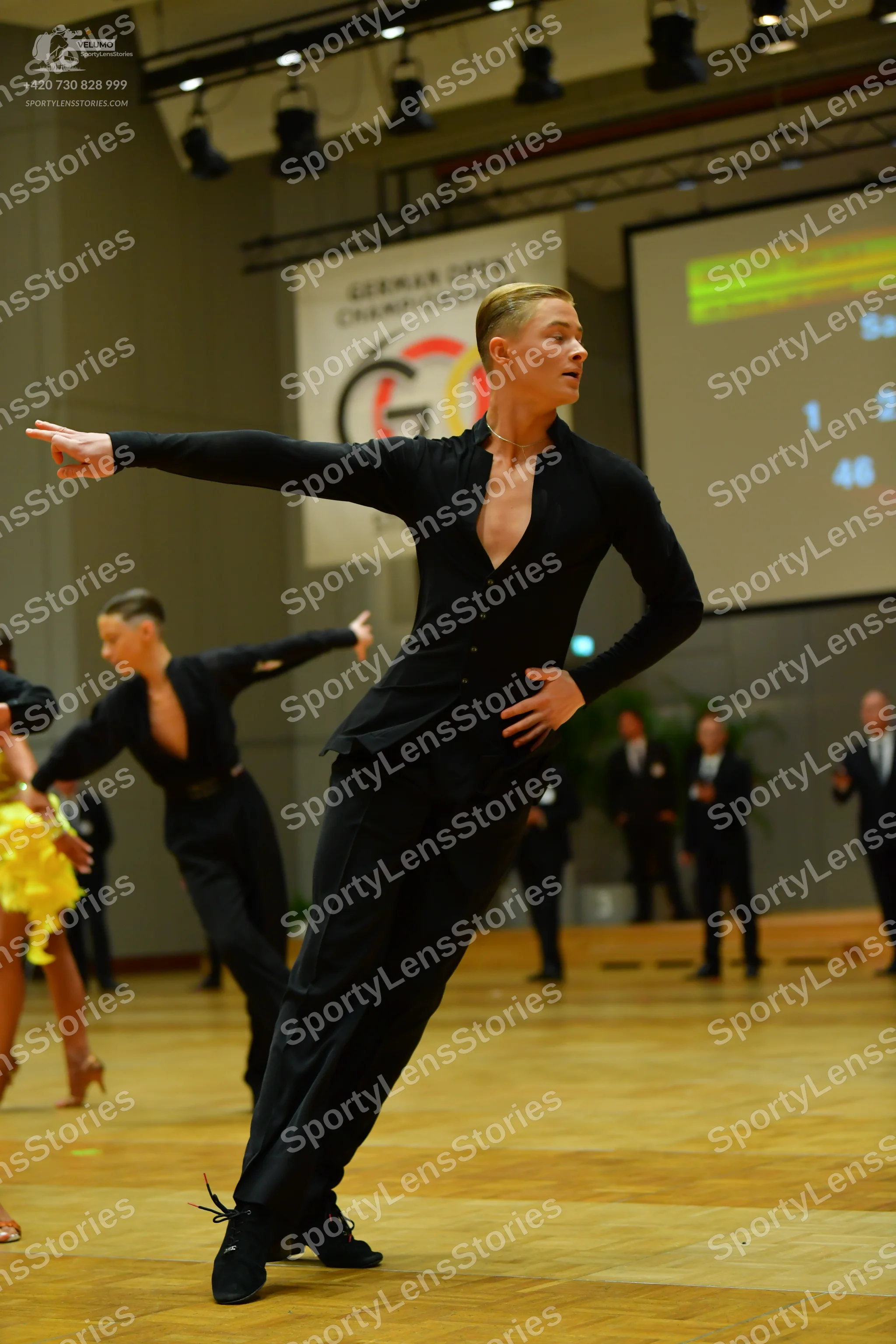 Dancesport competitor: Male dancer in foreground: black long-sleeved tight-fitting shirt with a deep V-