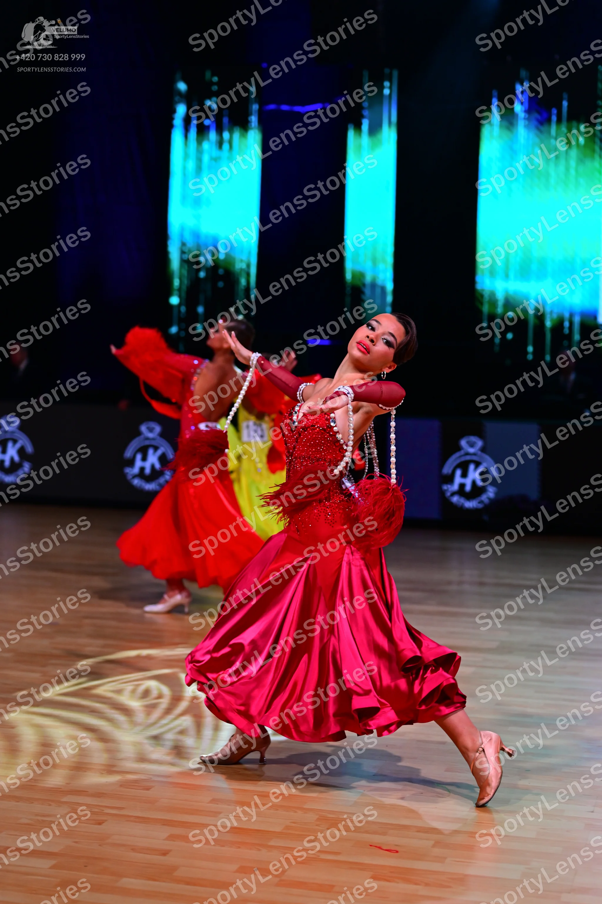Dancesport competitor: Female dancer in foreground: magenta satin ballgown with a red feathery bodice a