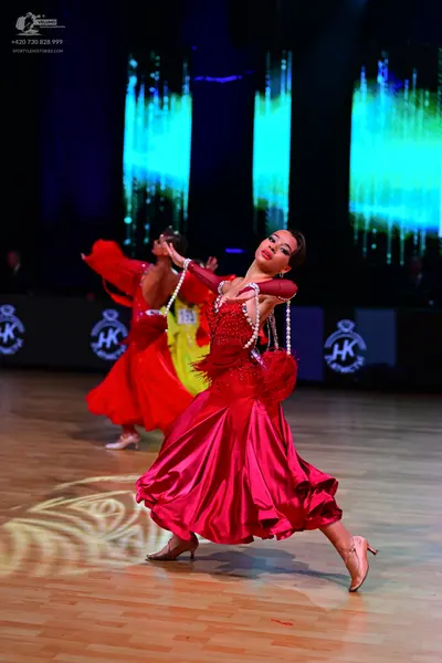 Dancesport competitor: Female dancer in foreground: magenta satin ballgown with a red feathery bodice a
