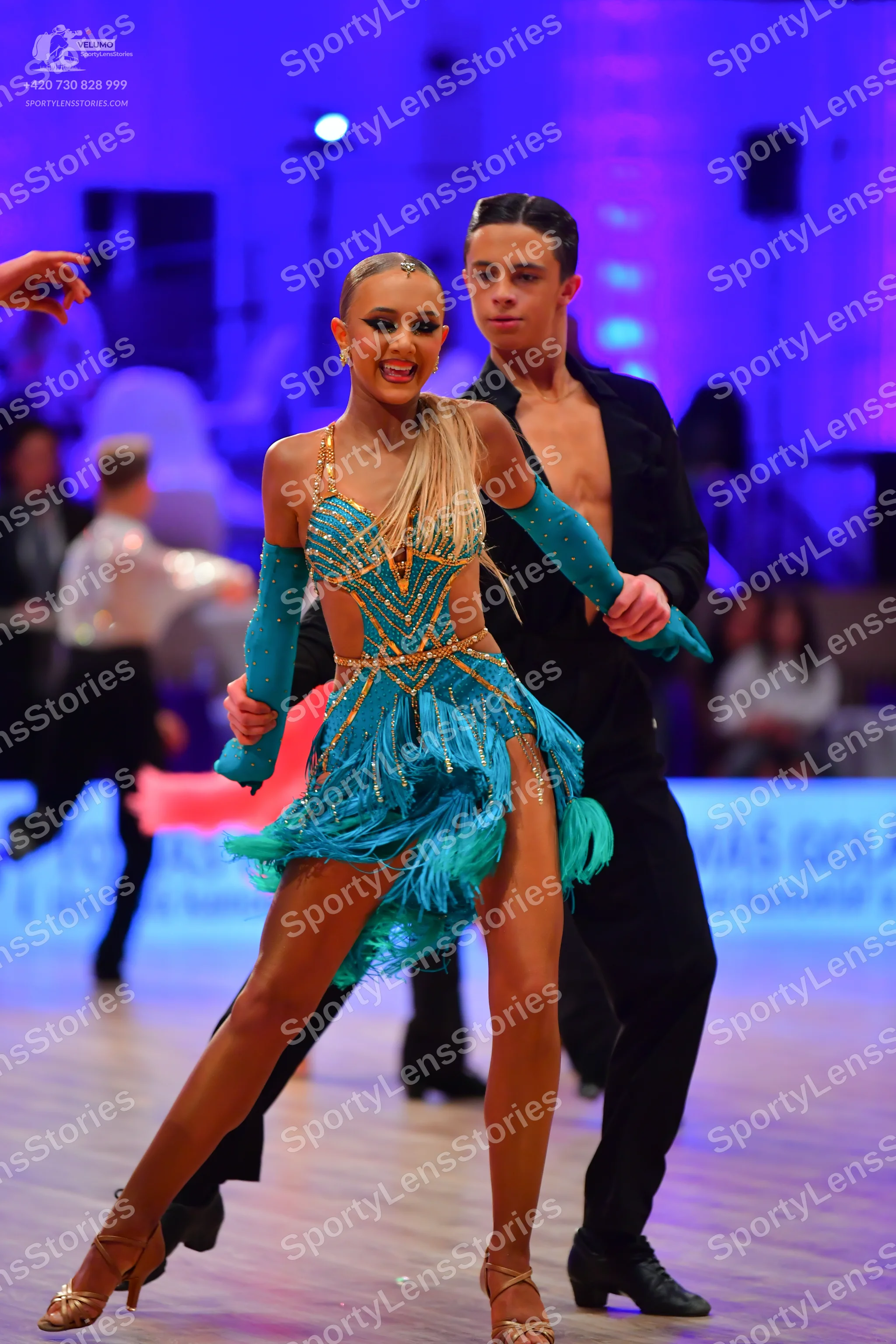 Dancesport competitor: Female dancer: turquoise Latin dance dress with gold sequin patterns, fringe on