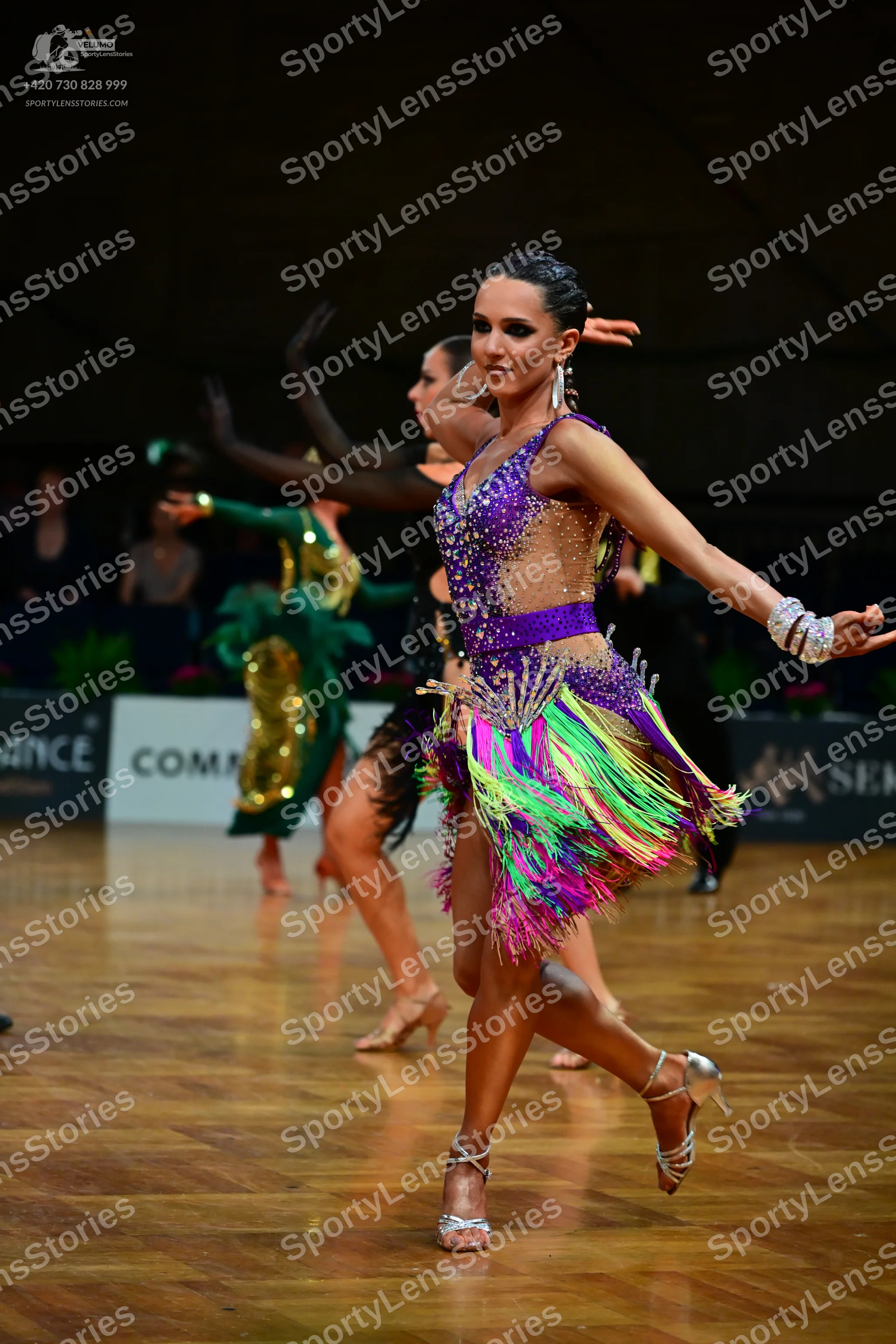 Dancesport competitor: Female dancer in foreground: purple Latin dress with sequins, sheer mesh panels,
