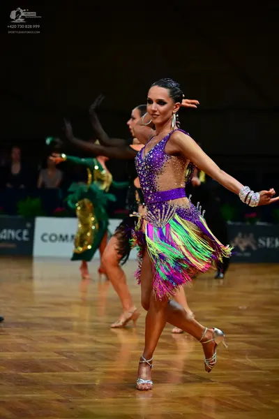 Dancesport competitor: Female dancer in foreground: purple Latin dress with sequins, sheer mesh panels,