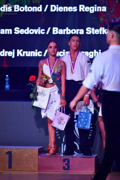 Dancesport competitor: Female dancer: white asymmetrical dress with colorful (gold, blue, red) lace or 