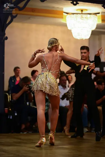 Dancesport competitor: Female dancer: gold sequined short Latin dress with thin straps and an open back