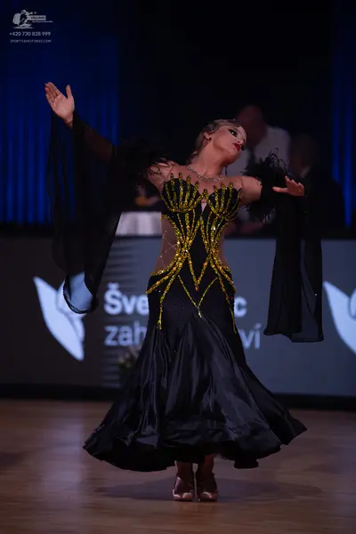 Dancesport competitor: Female dancer: black ballroom dress with a gold sequined bodice, long sheer blac