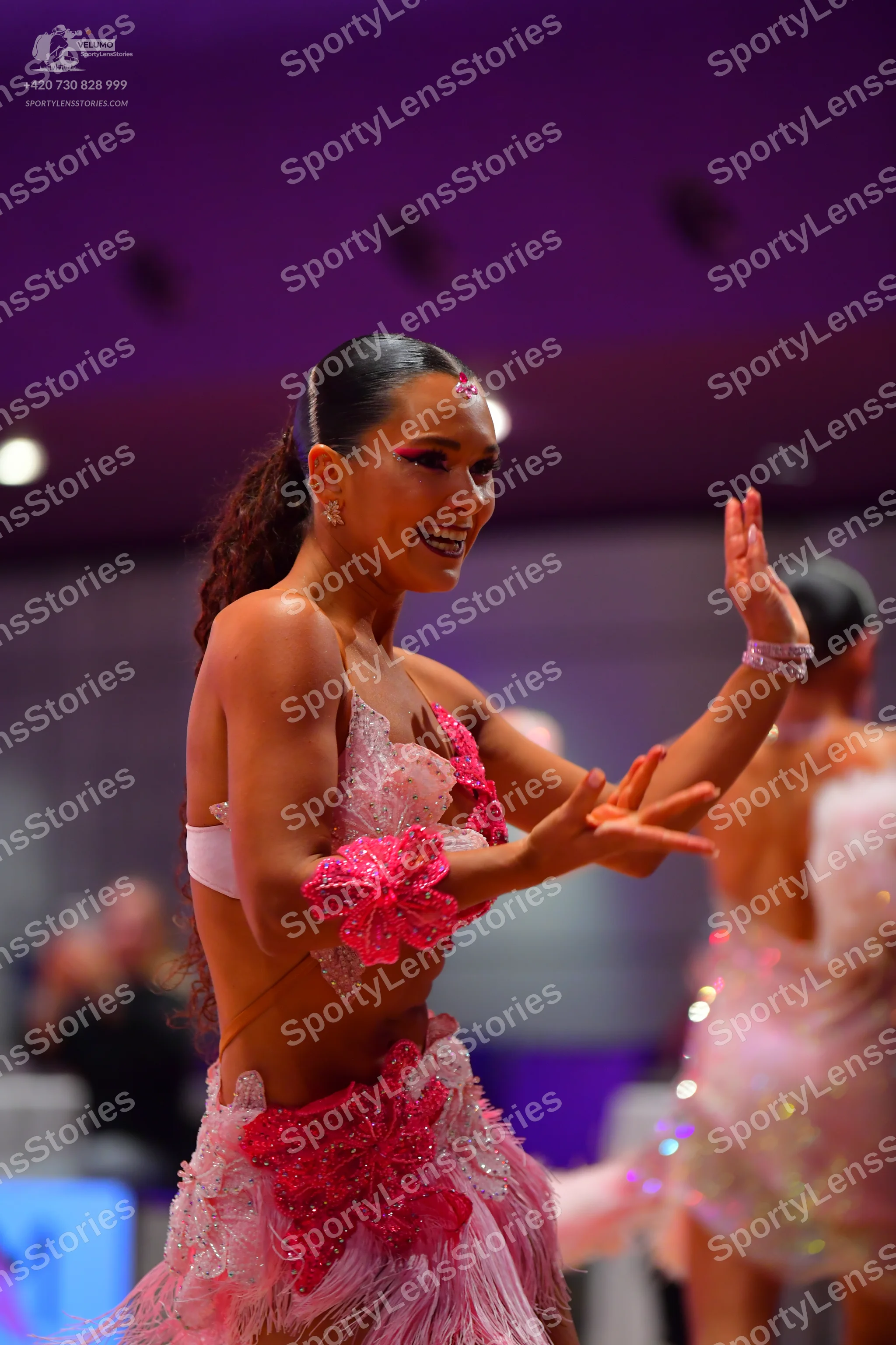 Dancesport competitor: Female dancer (foreground): pink Latin dance dress with bright pink sequined flo