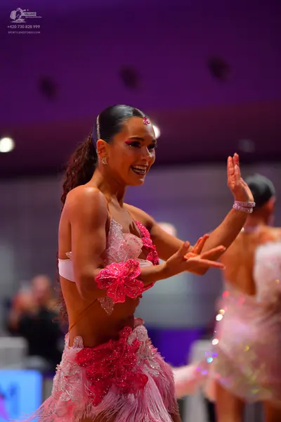 Dancesport competitor: Female dancer (foreground): pink Latin dance dress with bright pink sequined flo
