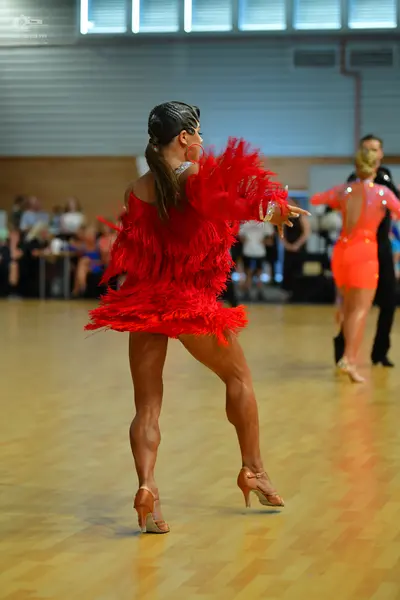 Dancesport competitor: Female dancer in foreground: red Latin dance dress with voluminous fringe