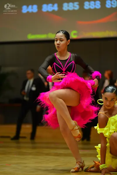 Dancesport competitor: Female dancer: pink latin dress with fringe and long black sleeves